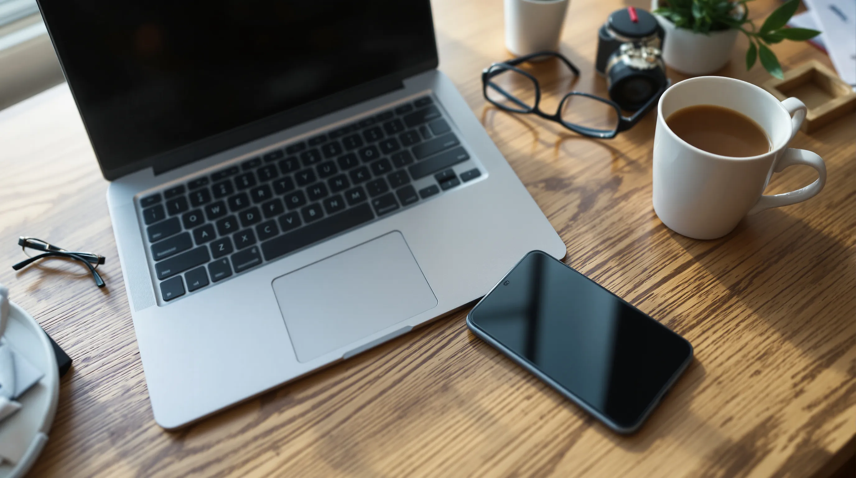 A desk with a laptop, smartphone and reading glasses viewed from above